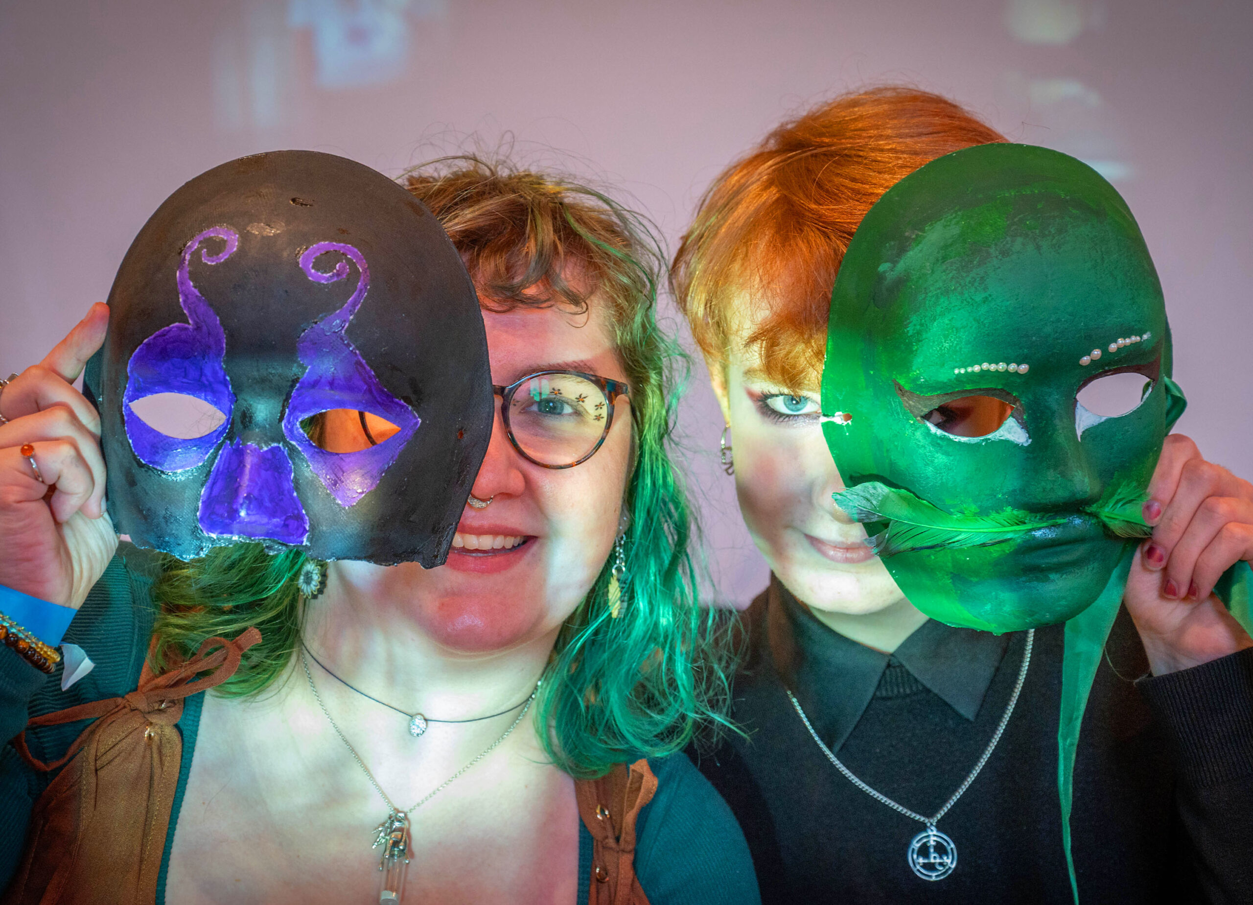 Two people holding theatre masks in front of their faces